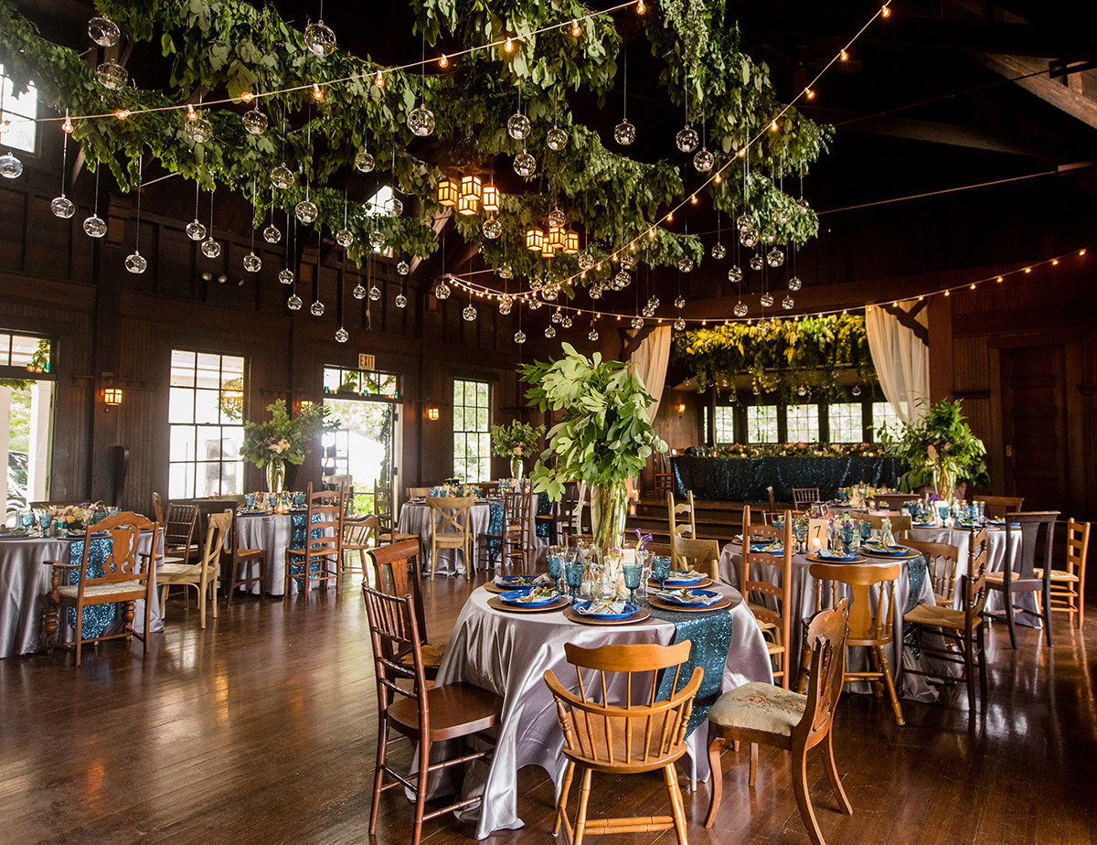 round tables set up for a wedding reception with greenery garlands, twinkle lights, and blue accents