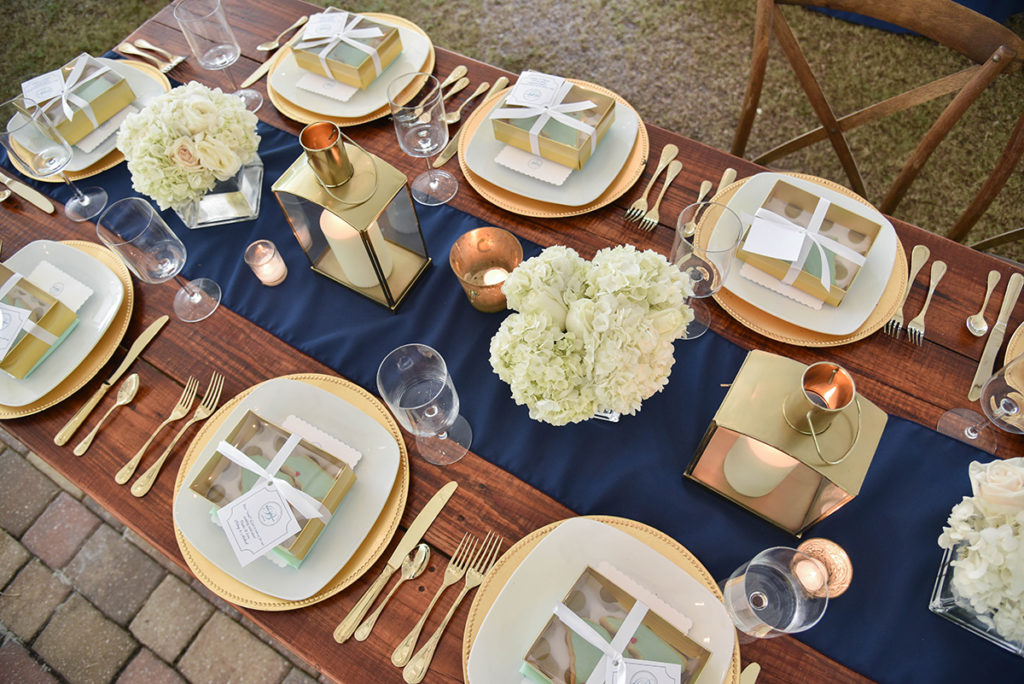 Wedding reception table shown from above with navy blue runner, gold decor accents and hydrangea bouquets