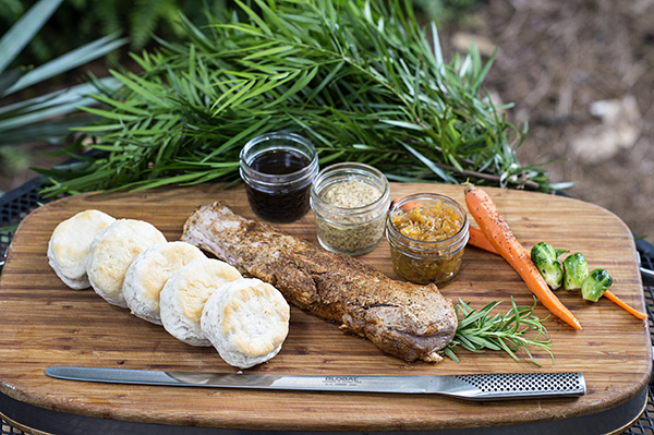 pork tenderloin and biscuits on a cutting board with various spreads in small glass jars